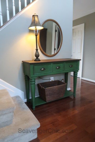 a green table with a mirror and lamp on top of it next to some stairs