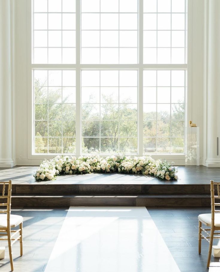 a wedding ceremony setup with white flowers and greenery in front of a large window