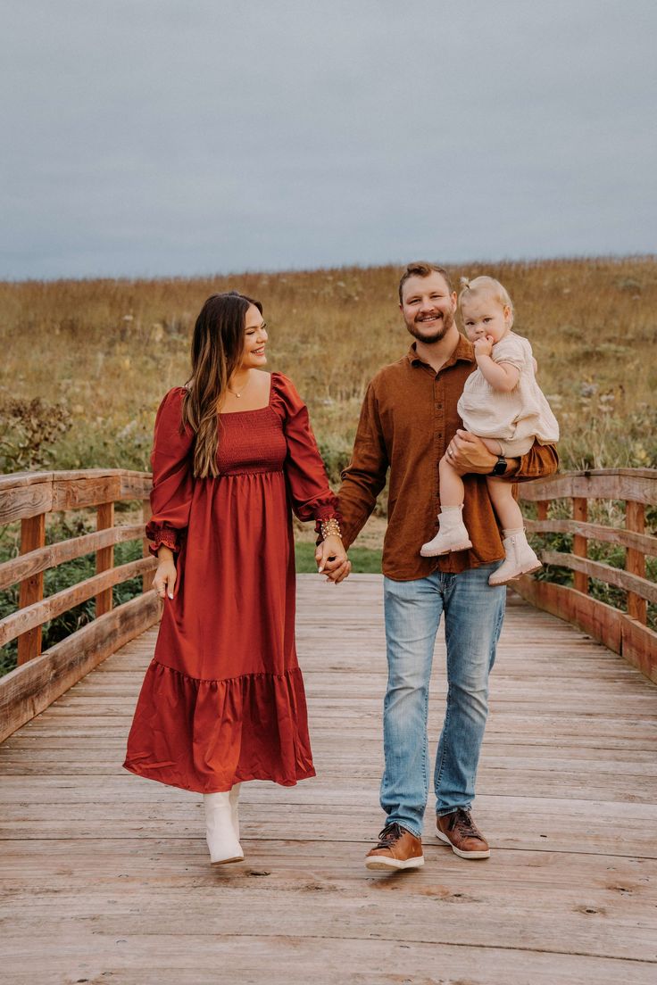 a man and woman holding hands while walking across a bridge with a baby in her arms