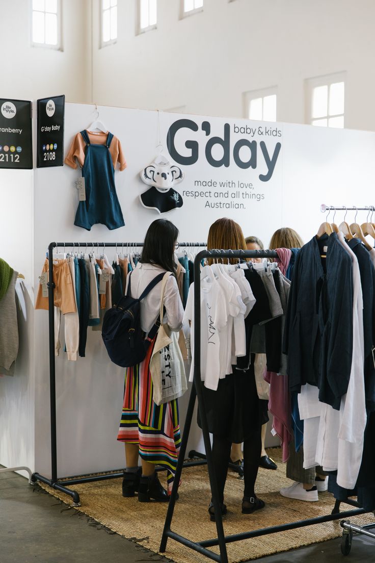 two women looking at clothes on display in a clothing store with an advertisement for the baby and kids's gdyy