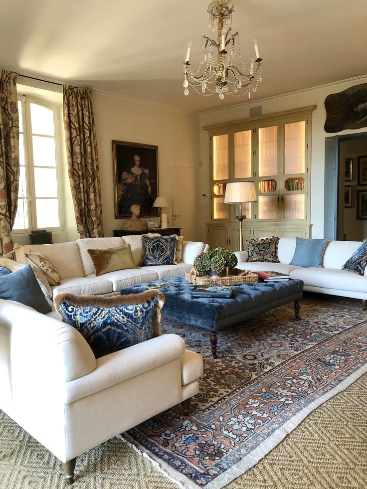 a living room filled with furniture and a chandelier hanging from the ceiling in front of two windows