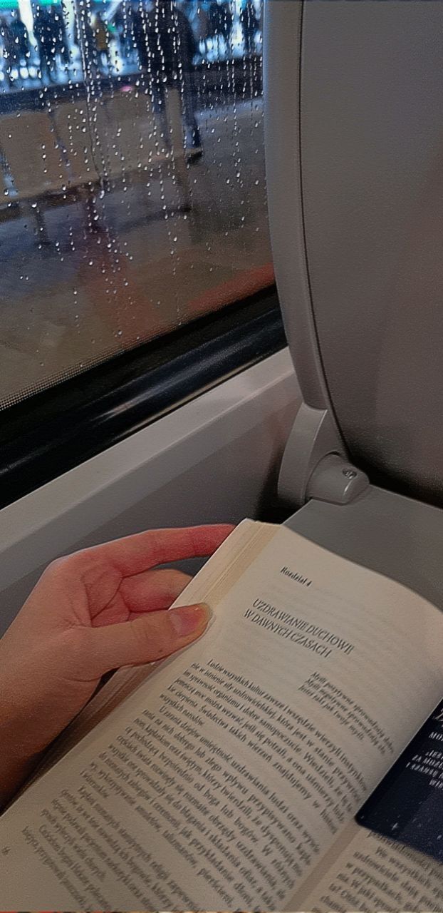 a person is reading a book on the train with rain coming through the window behind them