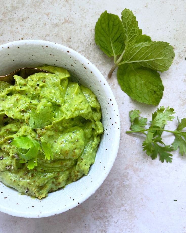 a white bowl filled with guacamole next to some green leaves and a spoon