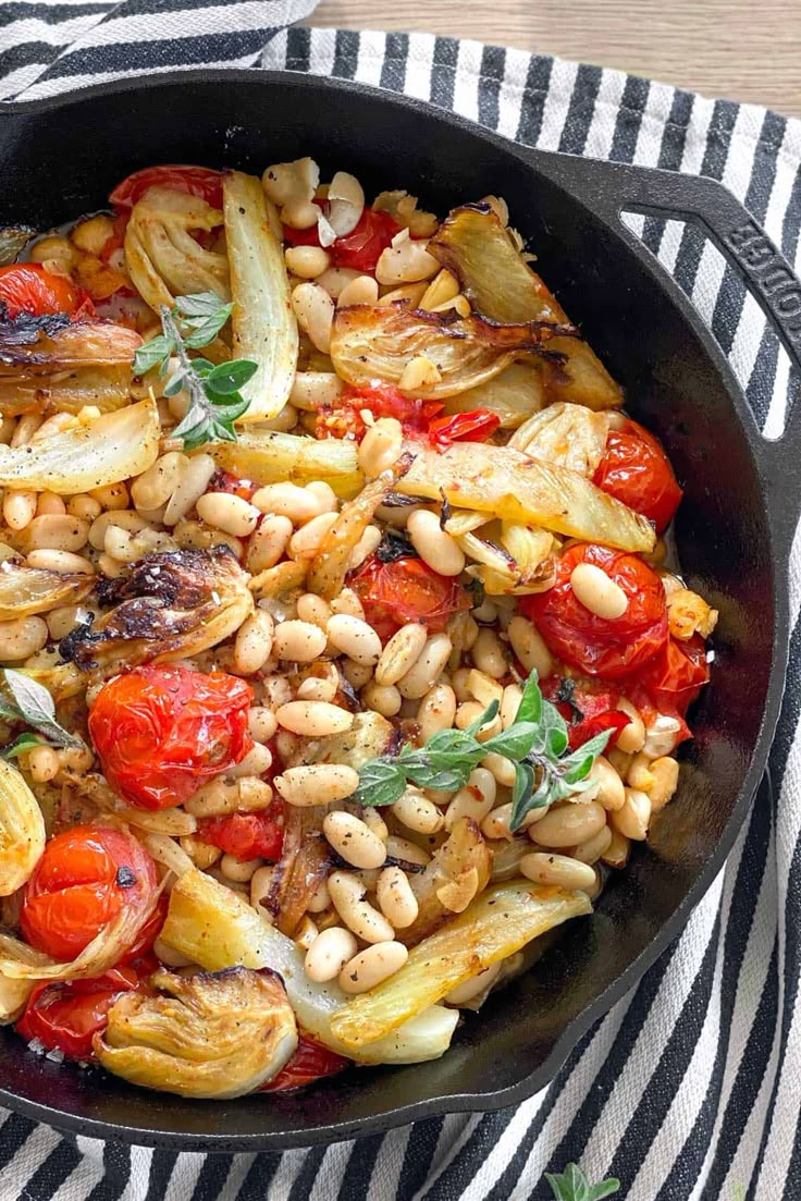 a skillet filled with beans, tomatoes and other vegetables on top of a striped cloth