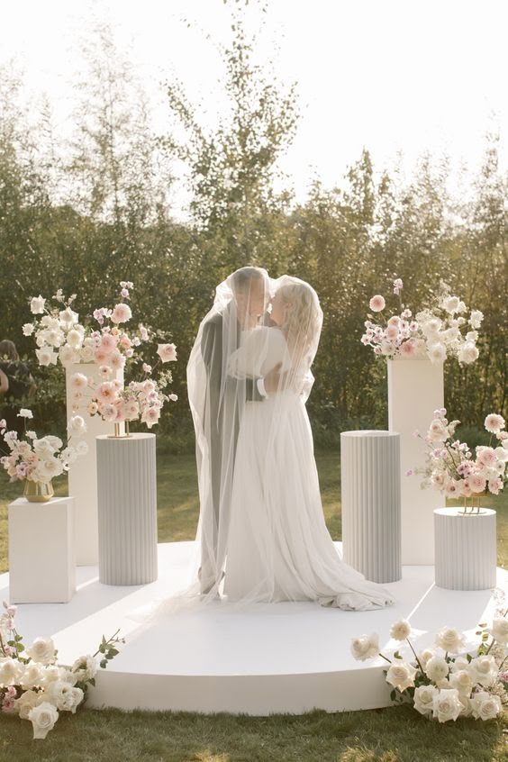 a bride and groom kissing in front of flower arrangements on a white pedestal with flowers