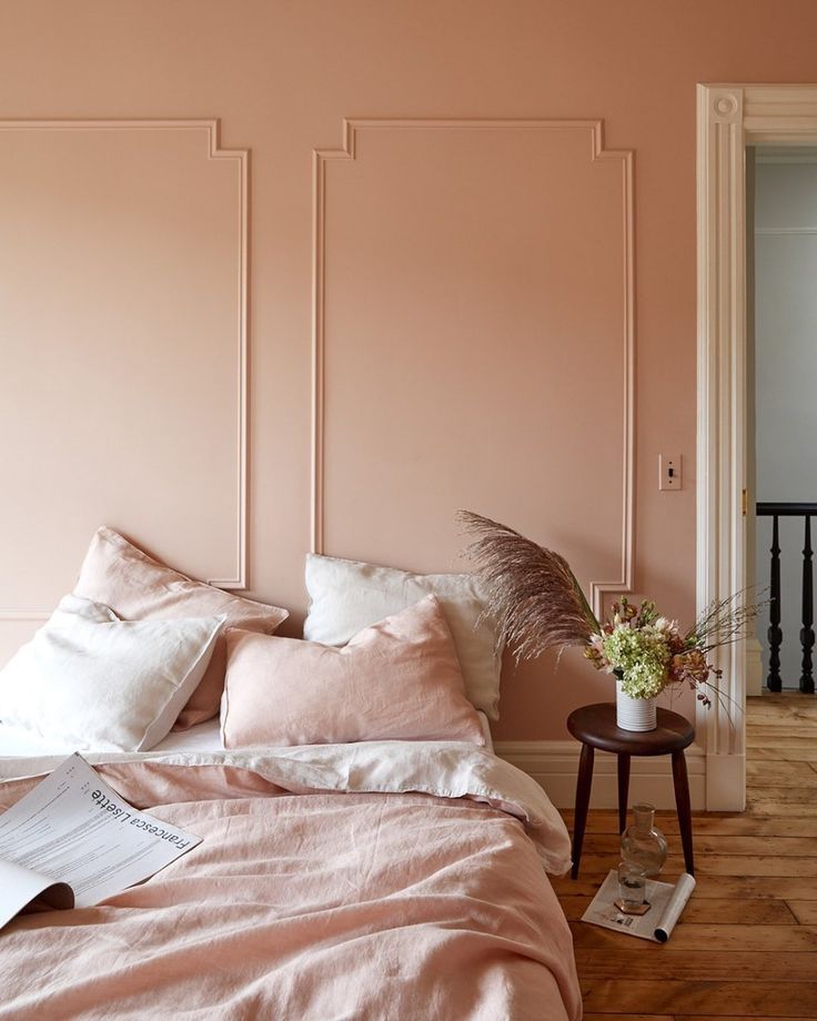 a bedroom with pink walls and white trim on the headboard, bedding and pillows