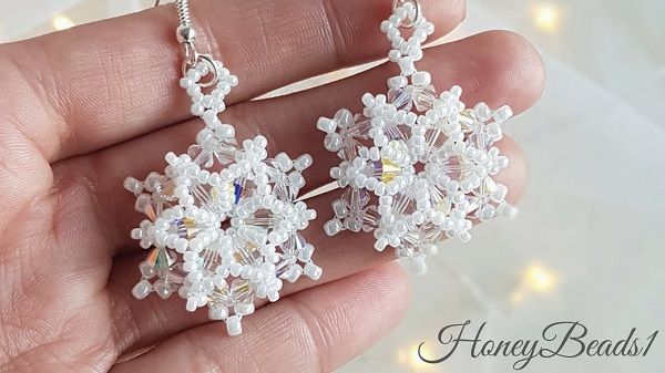 a pair of white beaded snowflake earrings on a person's hand