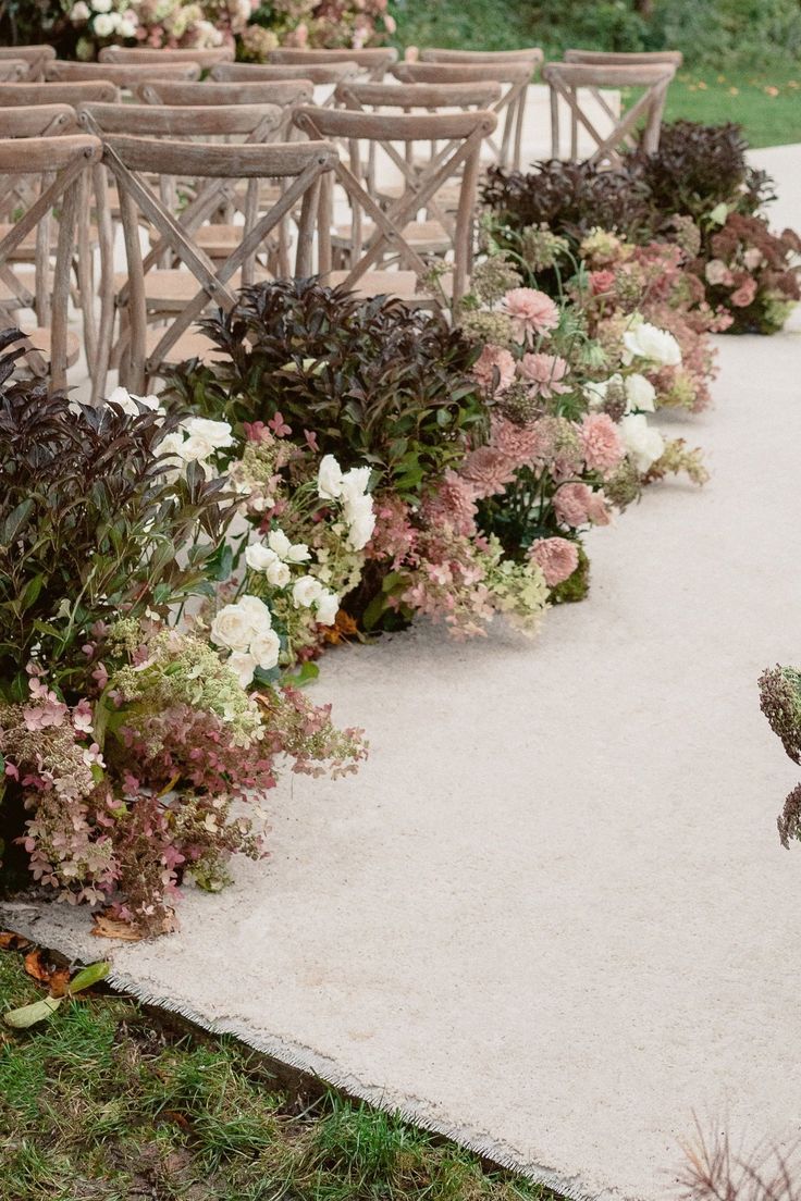 rows of wooden chairs with flowers lining the sides of them on a sidewalk in front of an outdoor ceremony area