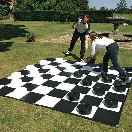 two people playing checkers on a giant chess board in the grass with another man watching