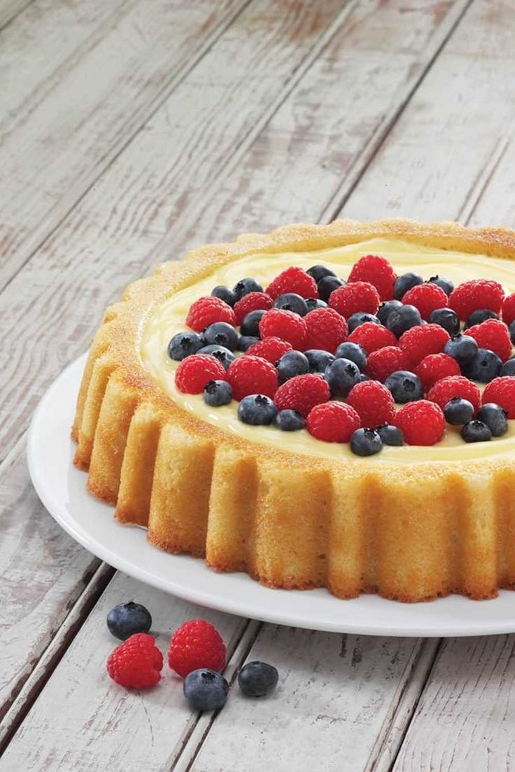 a cheesecake topped with berries and blueberries on a white plate next to raspberries