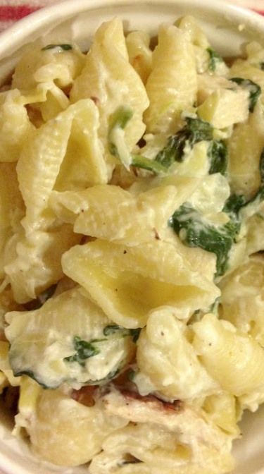 a white bowl filled with macaroni and cheese covered in spinach on top of a red checkered table cloth