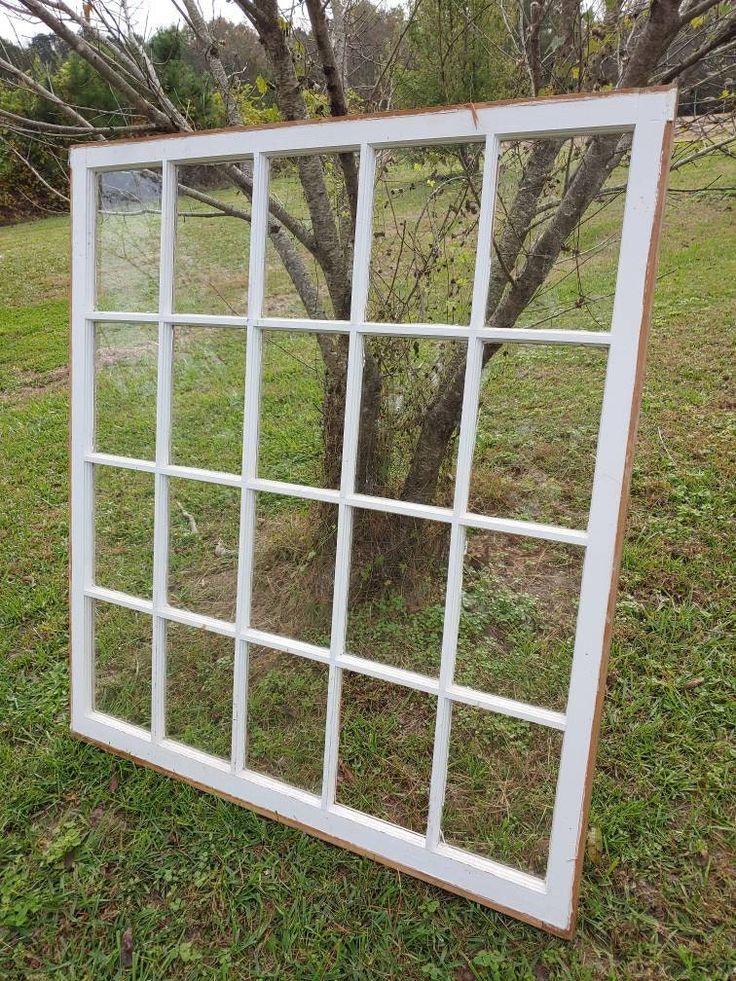 a white window frame sitting on top of a grass covered field next to a tree