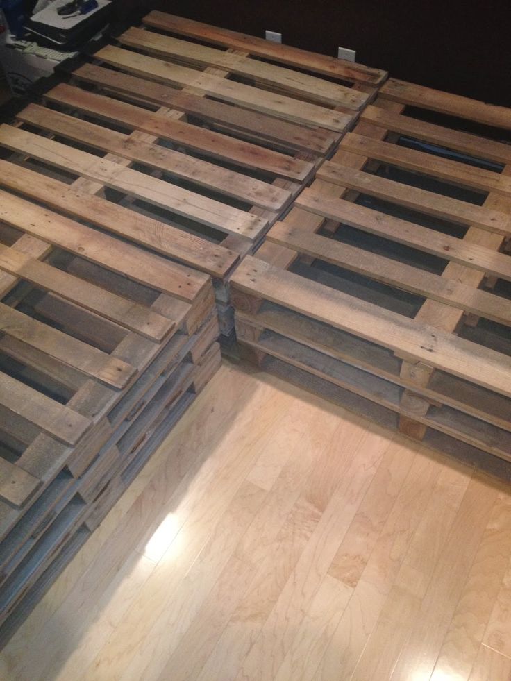 a bed made out of wooden pallets on top of a hard wood floor in a room