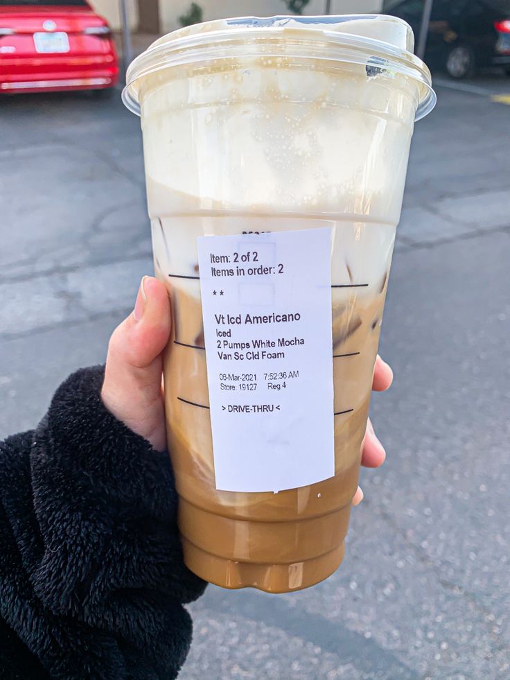 a person holding up a plastic cup with some liquid in it on the side of the road