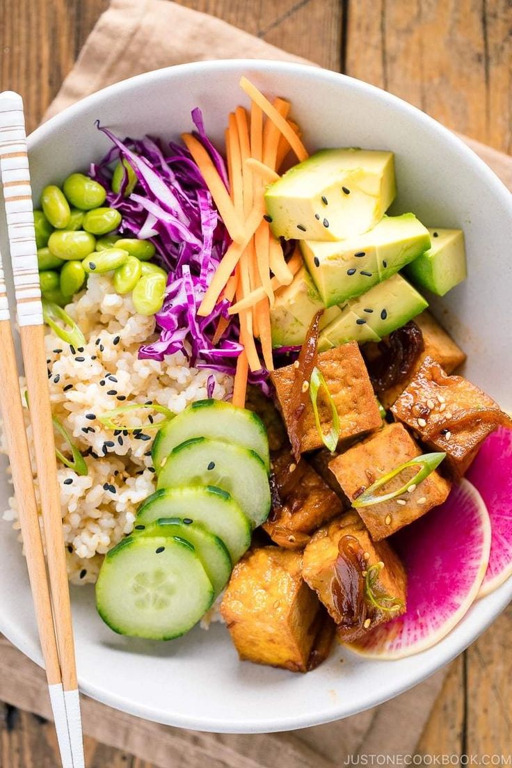 a bowl filled with rice, cucumber, carrots and other vegetables next to chopsticks