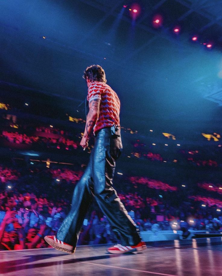 a male in a red and white striped shirt is walking on the stage at a concert