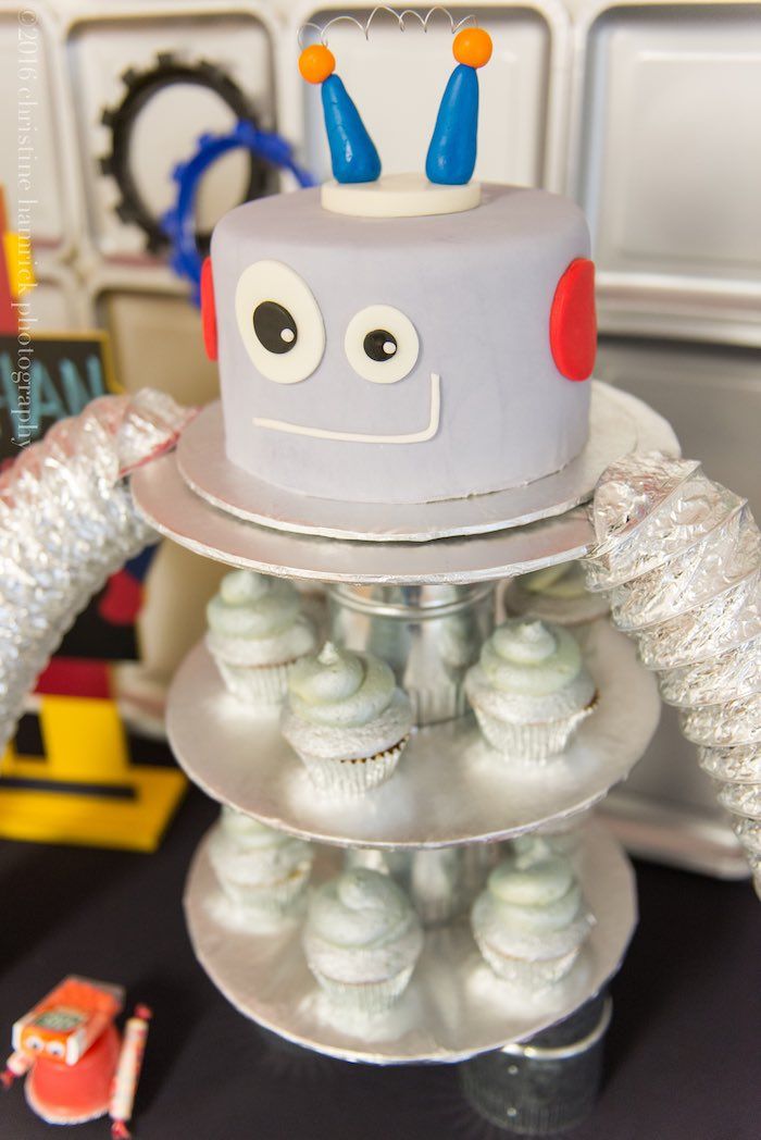 there is a cake that looks like a robot on top of some cupcakes