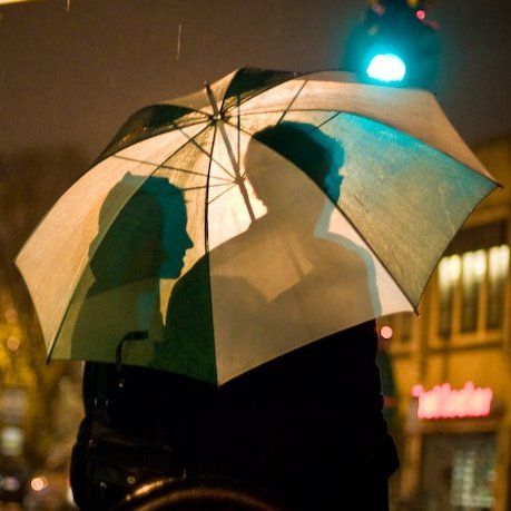 two people are standing under an umbrella in the rain at night, one person is holding an umbrella