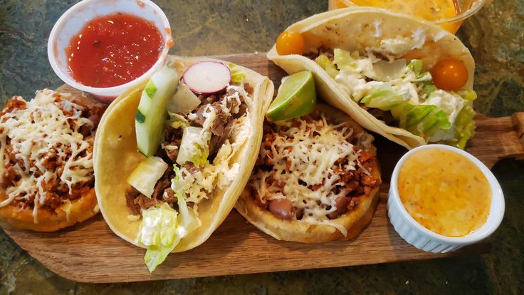 three tacos and some condiments on a wooden tray