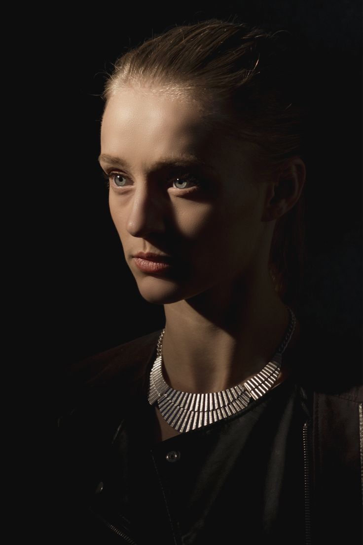 a woman wearing a black jacket and silver necklace in the dark with her eyes closed