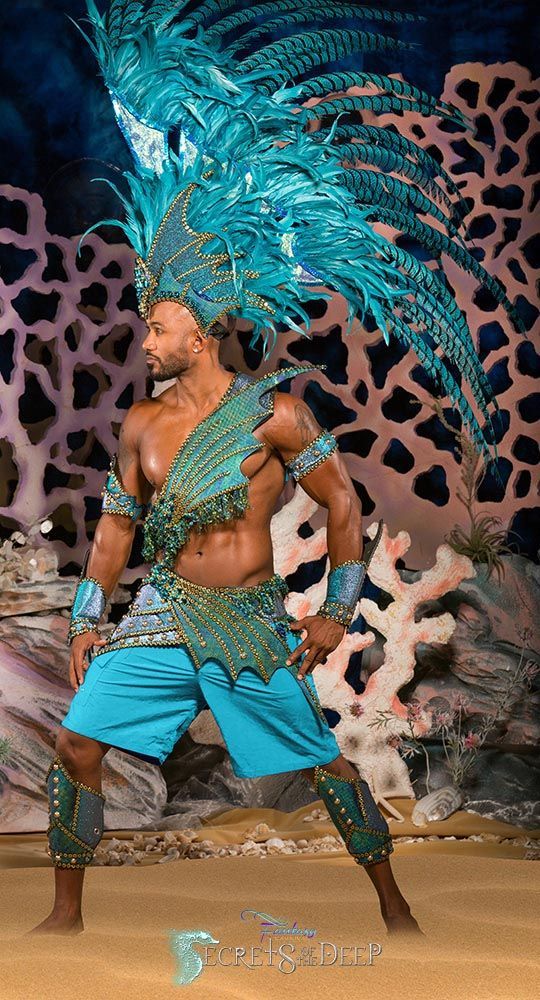 a man dressed in blue and green is dancing with feathers on his head while wearing an elaborate costume