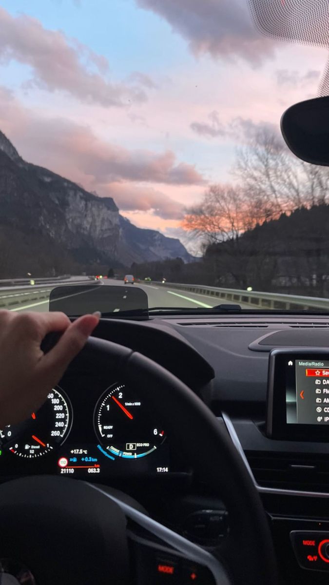 a person driving a car on a road with mountains in the background and a sunset