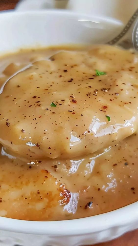 a spoon full of gravy sitting in a bowl on top of a table