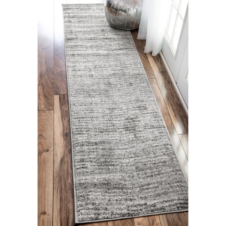 a gray rug on a wooden floor next to a window