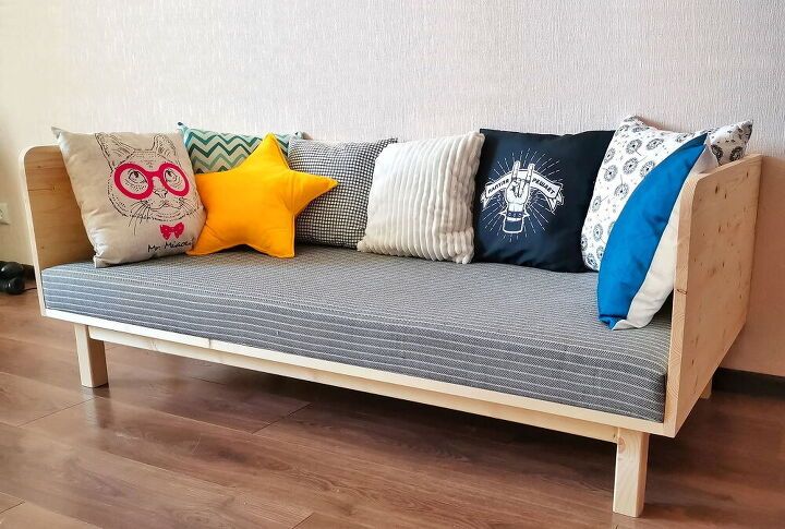 a couch with many pillows on it in front of a white wall and wooden floor