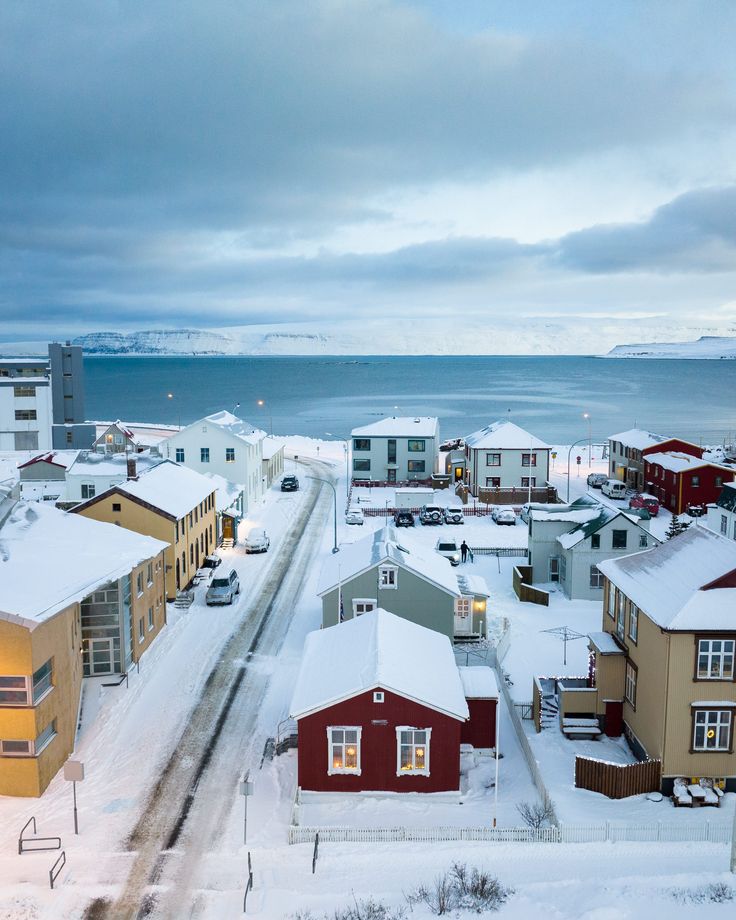 the snow covered streets are lined with houses and parked cars in front of the water