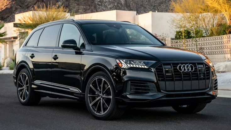 a black audi suv parked in front of a house with mountains and palm trees behind it