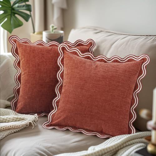 two red pillows sitting on top of a white bed next to a potted plant