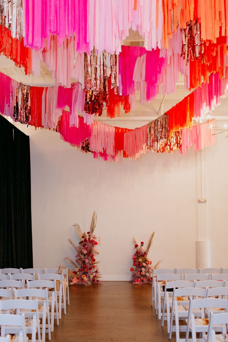 rows of white chairs with pink, red and orange streamers hanging from the ceiling