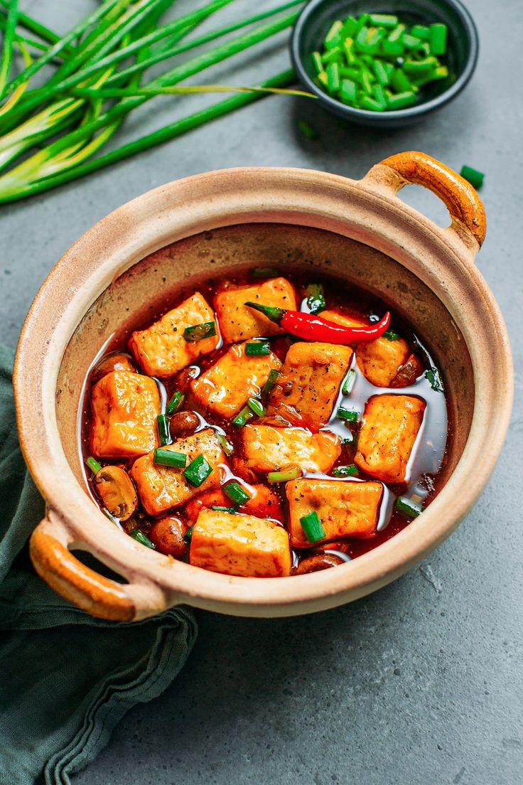 a bowl filled with tofu and vegetables next to some green onions on a table