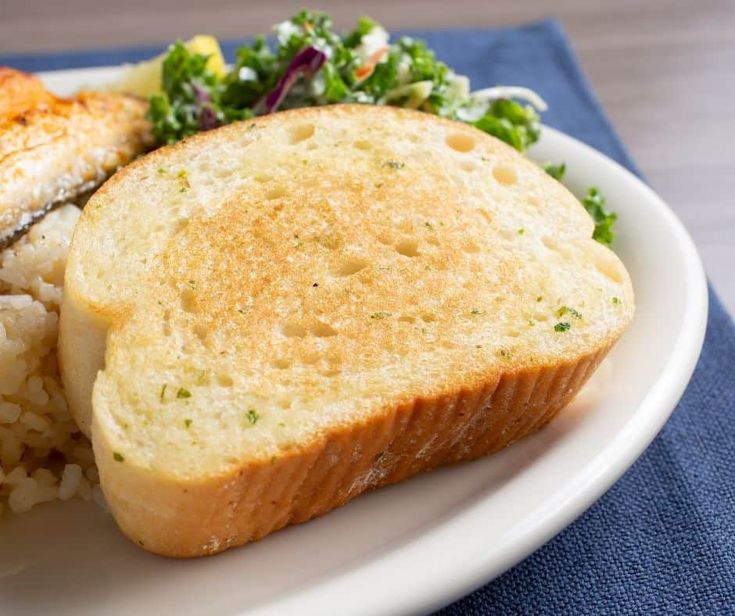 a white plate topped with bread and rice next to a green salad on a blue napkin