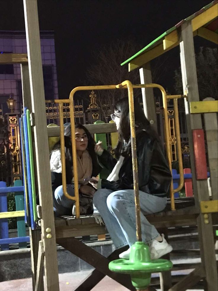 two people sitting on a playground at night