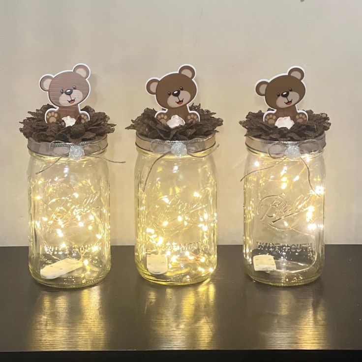 three mason jars with lights and teddy bears in them sitting on a table next to each other