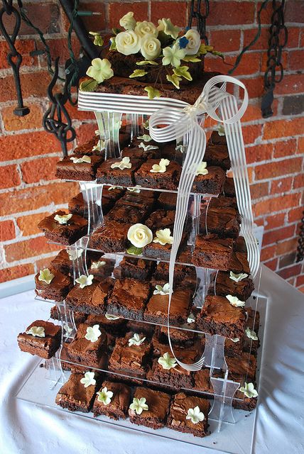 a tower of brownies with white flowers and ribbons on top is displayed in front of a brick wall