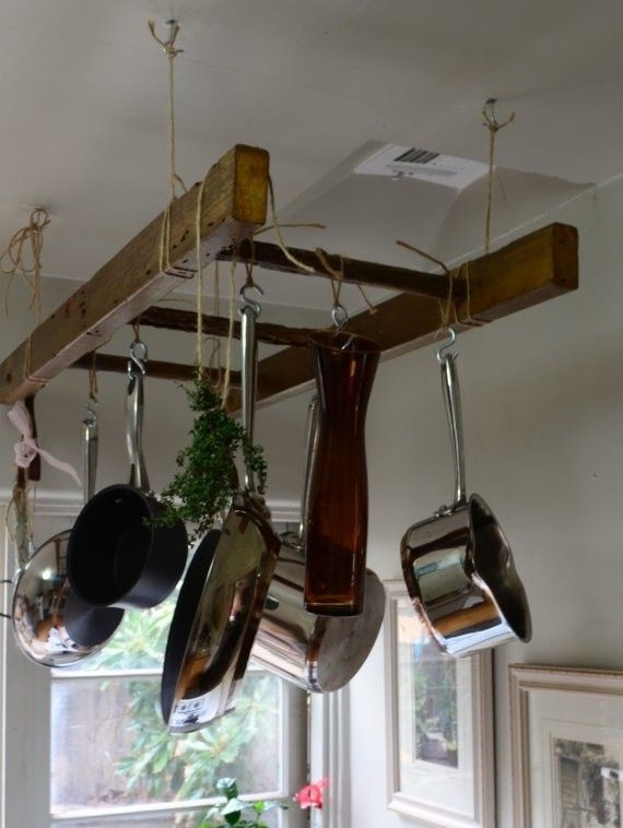 pots and pans hanging from a wooden rack in a kitchen with pot holders attached to the ceiling