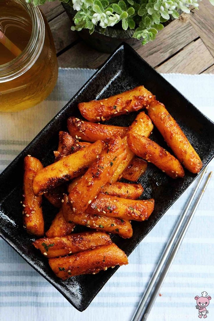 a black plate topped with fried carrots next to a glass of beer and chopsticks