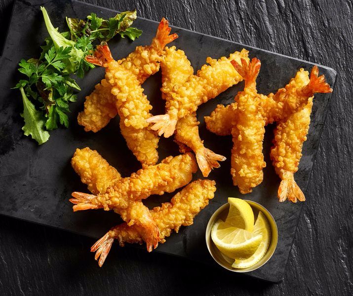 fried shrimp sticks with dipping sauce on a black plate next to lemon wedges and parsley