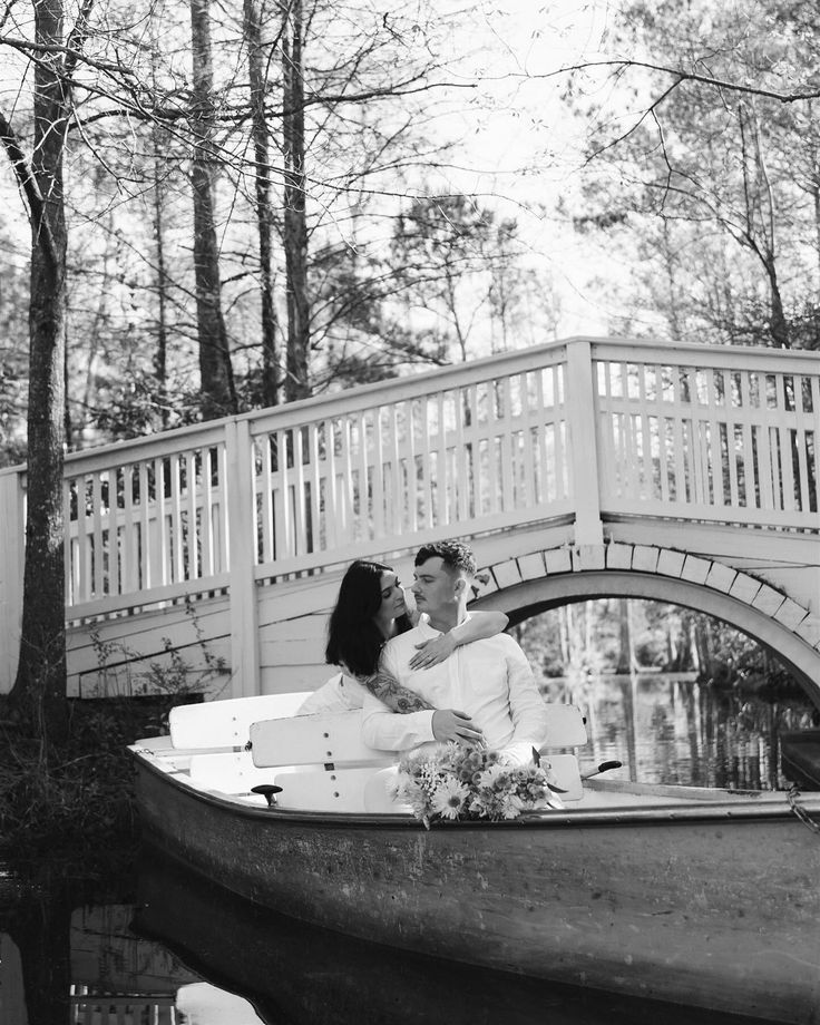 a man and woman are sitting on a boat in the water with bridge behind them