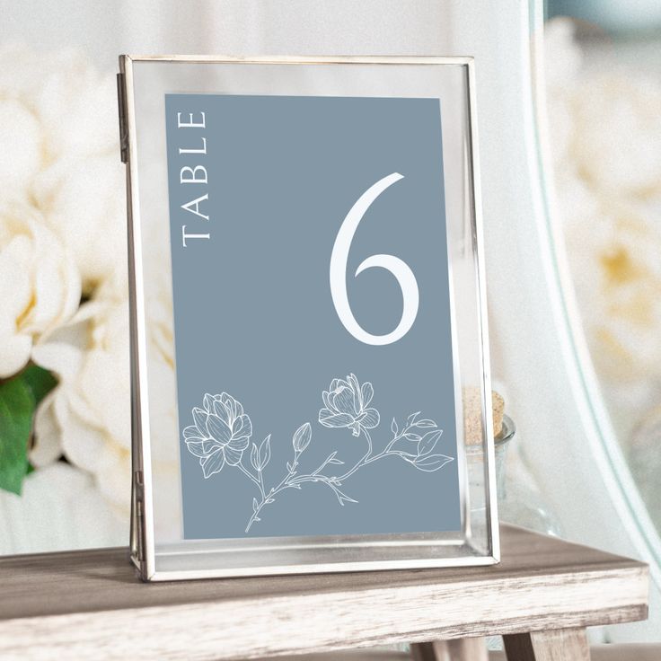 a table number is placed on top of a wooden table with flowers in the background