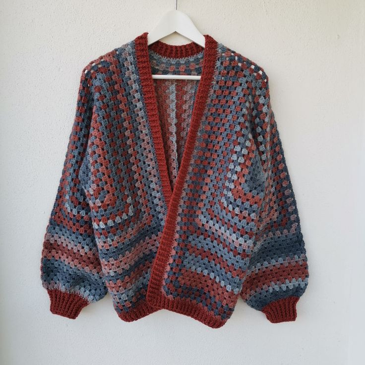 a crocheted cardigan hanging on a wall with a hanger in front of it