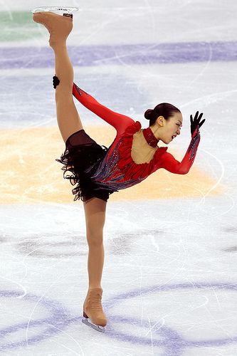 a female figure skating on the ice in a red and black outfit with her arms outstretched