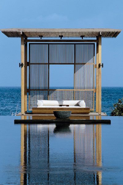 an open air swimming pool next to the ocean with a lounge chair and umbrella on it