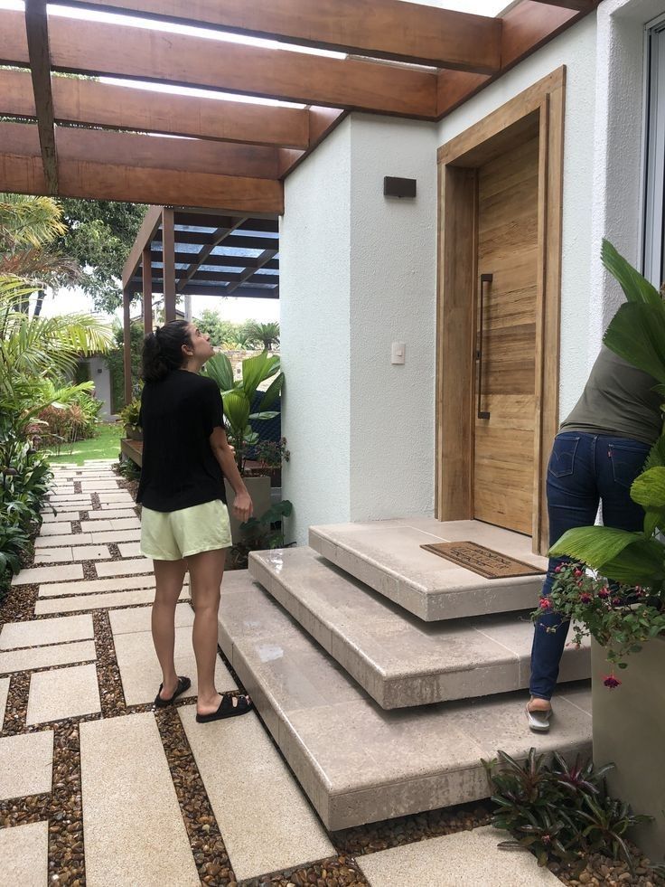 two women standing on steps in front of a house with wooden door and planters