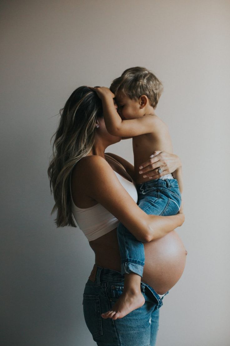 a pregnant woman is holding her son's head while he kisses the belly of his child