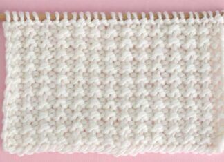 a close up of a white crochet stitch on a pink background with a wooden needle