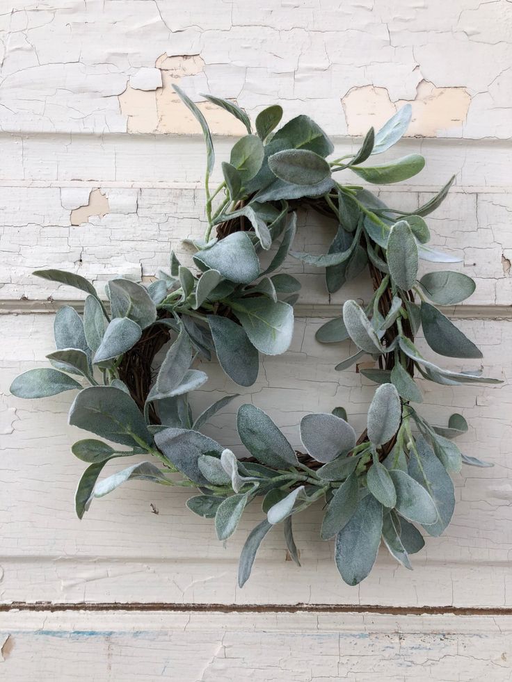 a wreath made out of eucalyptus leaves on a white painted wooden door with peeling paint